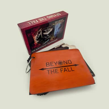 Beyond The Fall Survivalist Compendium box set displayed with a laser-engraved orange wooden ring-bound reference guide, showing the branded compass logo cover alongside the product box featuring wilderness survival imagery against a light gray background.